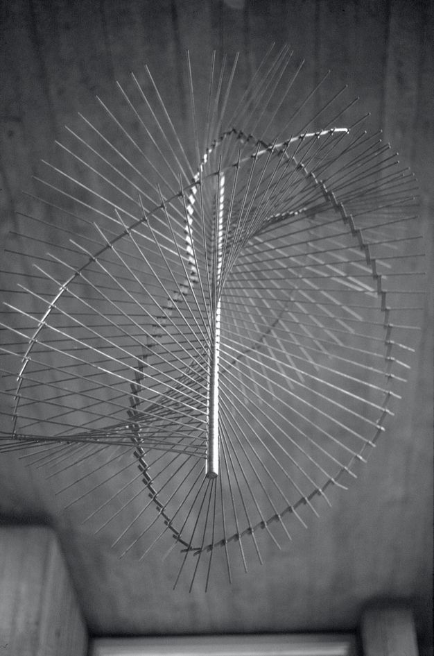Metal sculpture. Mobile consists of a central vertical bar with hundreds of thin metal rods extending out in all directions to create an interlocking spiral wave.
