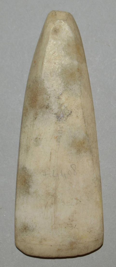 A close-up of an elongated, carved ivory or bone artefact with a smooth, tapered shape and visible wear marks.