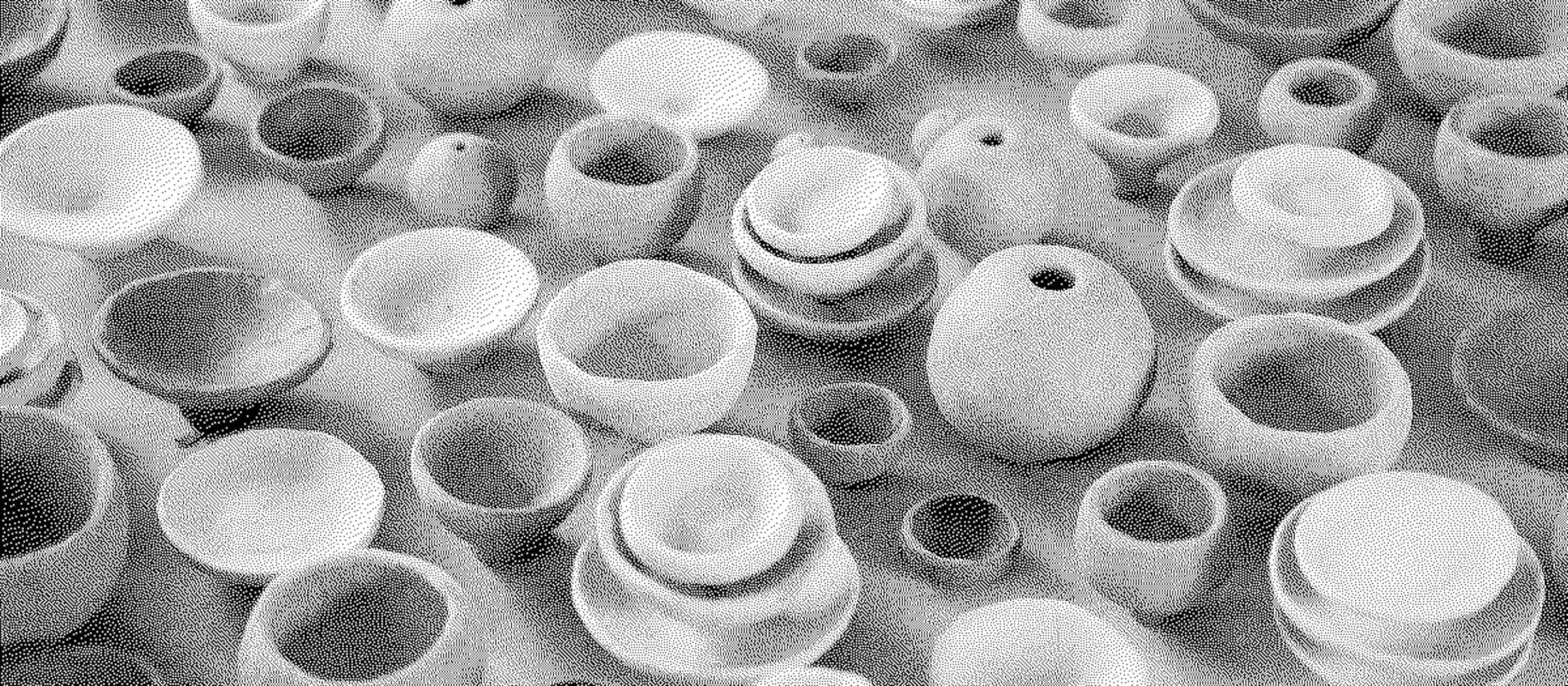 A collection of small handmade ceramic bowls and vessels in earthy tones, displayed on a wooden surface. The pieces vary in size and shape, with some stacked and others scattered.