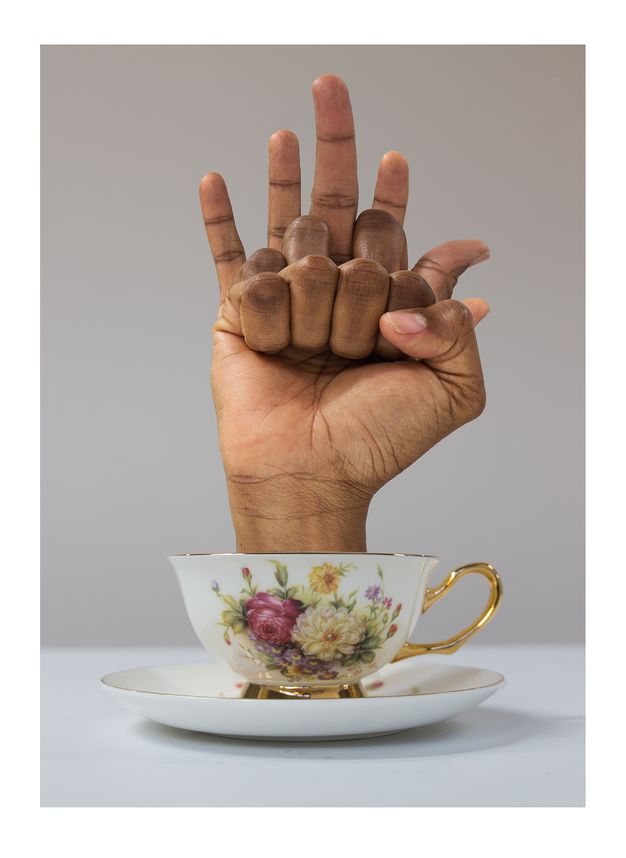 Another version of the teacup artwork, with the hand now partially curled into a fist, the fingers appearing to fold inward in an unusual manner.