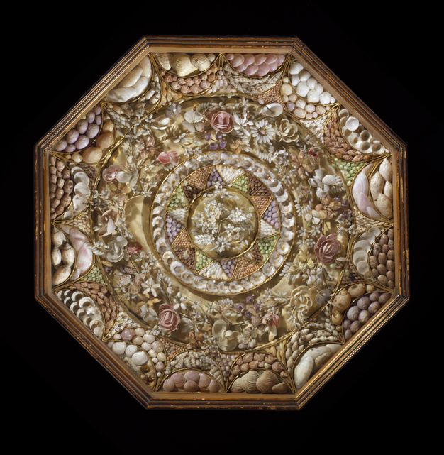 An ornate sailor’s valentine encased in glass, showcasing an elaborate symmetrical design made of small shells, including floral motifs, a central wreath, and pastel-coloured patterns.
