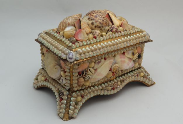 A decorative wooden shellwork box covered in various types of seashells, including larger conch shells and smaller beads, with a hinged lid.