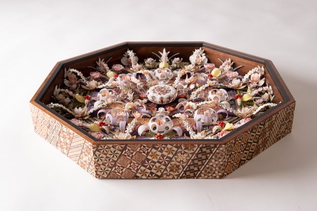 A side view of an octagonal shellwork shadowbox with intricate floral and geometric patterns made from shells, set inside a wooden frame with decorative inlays.