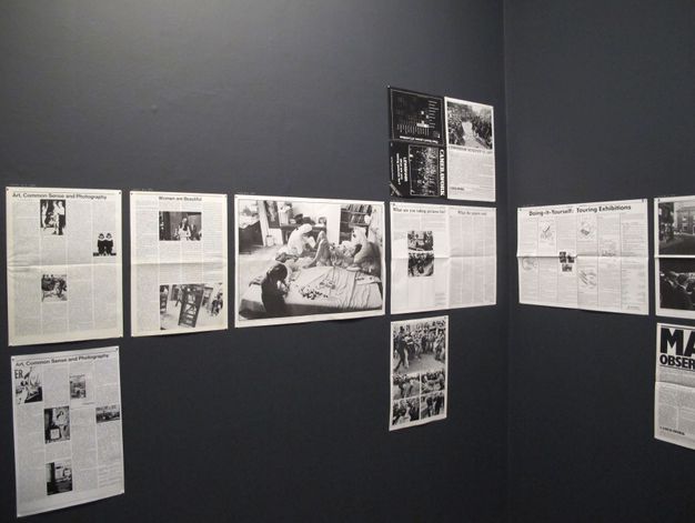 Exhibition wall displaying a series of black-and-white and text-based posters. The posters include articles and photo essays, with titles such as "Art, Common Sense and Photography" and "Women are Beautiful." The images comprise both textual content and photographs depicting various scenes, possibly related to the themes of art and cultural exhibits. The arrangement is done on a dark gray wall, suggesting a museum or gallery setting focused on visual and textual analysis.