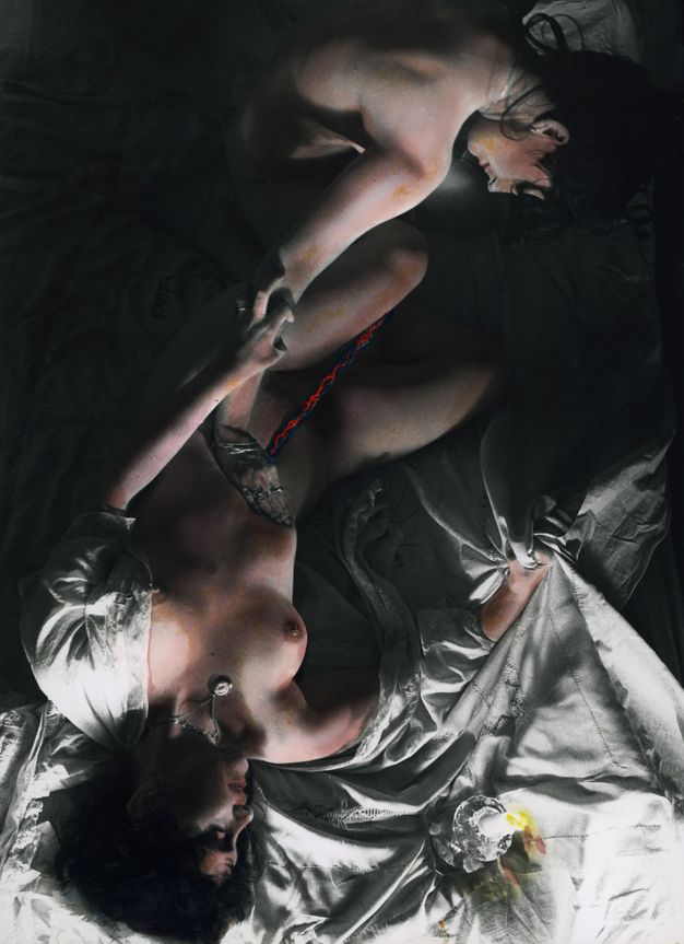 Colour photograph. Two naked women lying opposite each other on top of bed covers, one woman digs her nails into the other's arm and the bedsheet, the second woman holding her counterpart's stomach. Red and blue wires extrude from the first woman's stomach, while a lit candle occupies the lower-right corner.