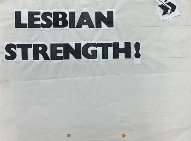 Black and white photograph. This photograph documents the mock up for a flyer, with cut-out, individual black and white letters pasted on a white sheet of paper reading, “LESBIAN STRENGTH”. A stack of further cut-out symbols is attached to the paper on one corner by a paperclip.