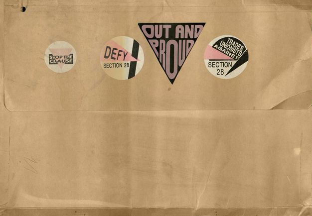 Colour photograph. In this colour photograph a brown storage folder features a series of four stickers adorned with different sections of text. Two are related to the defiance against section 28, while the other two read, “OUT AND PROUD”, and “STOP THE CLAUSE”.