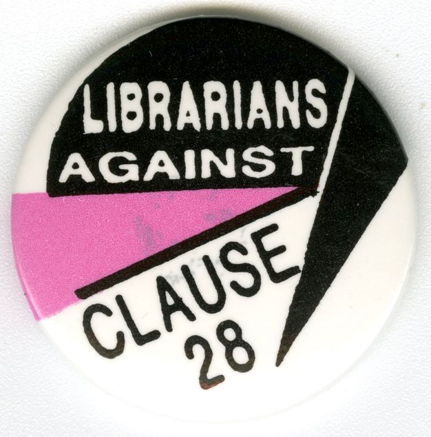 Colour photograph. This colour photograph documents a circular pin badge decorated with an angular pink, black and white logo which is interwoven with the bold typeface text, “LIBRARIANS AGAINST CLAUSE 28.”