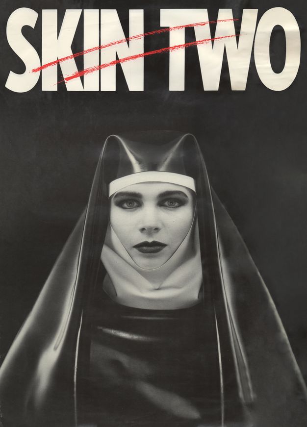 Cover of a magazine. A person wearing heavy makeup and a nun’s habit made from rubber-like fabric is set against a black background. Above them white text reading ‘SKIN TWO’ is scored across with two red, horizontal slashes.