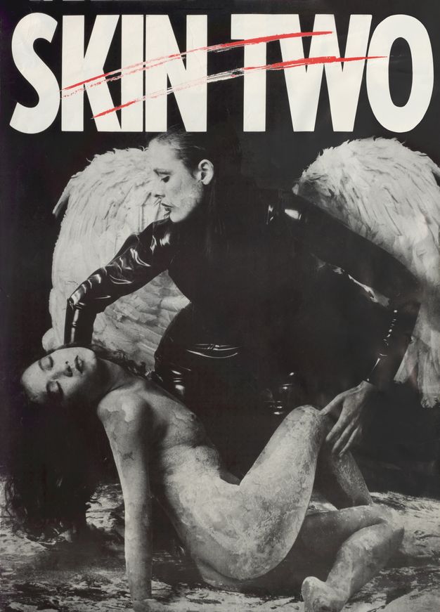 Poster. A person dressed in fitted, black patent leather clothing wears large white angel wings. They kneel down to lift the reclining body of another person who is naked and covered in a white, paint-like substance. Above them white text reading ‘SKIN TWO’ is scored across with two red, horizontal slashes.