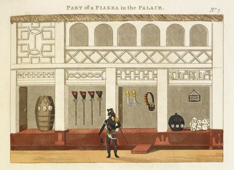 Drawing. A colour drawing documenting one wall of a piazza. The wall contains tall white pillars, above which are carved panels and archways. Various objects in the four open spaces between the pillars include a stack of white skulls, and weapons. In front of the building, a black, half-dressed man wears colourful clothing and has a spear on his back. Above the drawing reads the text, ‘Part of a Piazza in the Palace.’