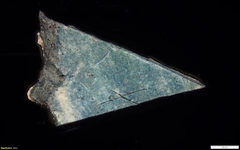Colour photograph. Magnified photograph of a rock or mineral in turquoise, showing a close-up view of its surface and texture against a black backdrop.