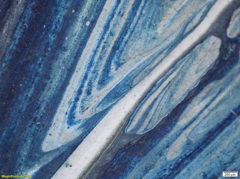 Colour photograph. A close-up, detailed study of a textural area of paint, featuring shades of blue, grey, and beige, with a glossy appearance. On the lower left yellow text reads, ‘Magnification: 0.67’. On the right, a small white rectangle bears the text ‘2 mm’.