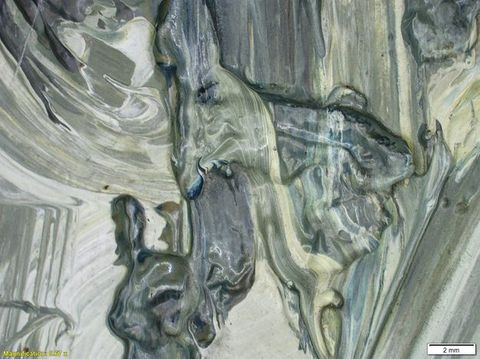 Colour photograph. A close-up, detailed study of a textural area of paint, featuring shades of beige, grey, and white, with a glossy appearance. On the lower left yellow text reads, ‘Magnification: 0.67’. On the right, a small white rectangle bears the text ‘2 mm’.