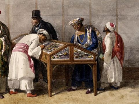 Painting. A group of people stand in an interior space around a wood and glass cabinet case, with two leaning in for a closer look. Within the case we can see an array of brightly-coloured objects. Four of the people wear long and loose, belted tunics, while another in the distance is dressed in a black coat and a traditional top hat. 