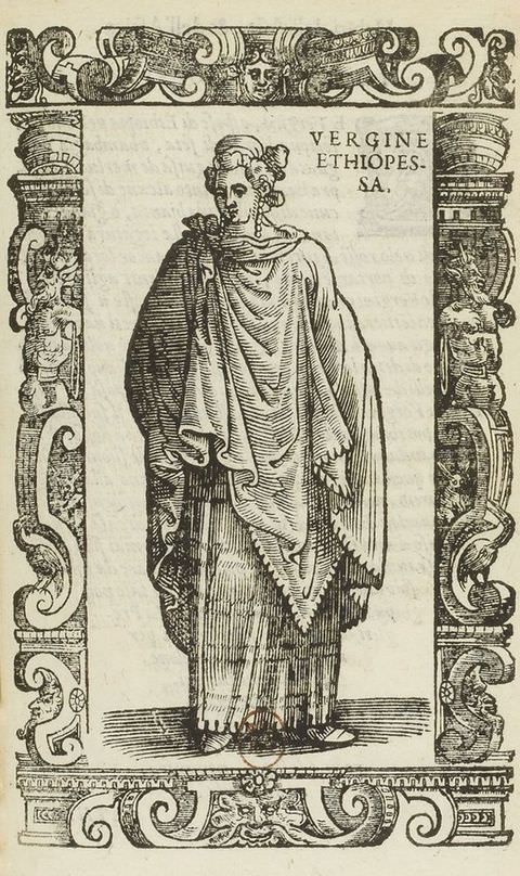 Page of a book. This black and white book illustration is surrounded by an ornately decorated frame featuring three-dimensional, organic shapes. Within the frame stands a figure dressed in long, draped fabric with a tie on their right shoulder. Text on the upper right of the image reads ‘VERGINE ETHIOPES. SA.’