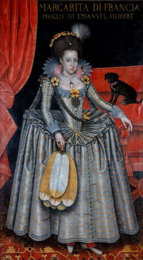 Painting. A woman is dressed in an elaborate, historical dress, with a corseted waist, full, long skirt, and lace collar. In the dark room behind her, a thick, red curtain is swept to one side, while on the left a small black dog sits on a red sofa. The floor she stands on is decorated with an ornate red and yellow pattern, while text above reads, ‘Margarita di Francia’.
