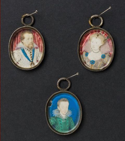 Colour photograph. A document of three circular miniature portraits on a black backdrop, each hung by a loop on a long nail. The top two are placed side-by-side, with the left featuring a man, and the right, a woman. Below them in the centre is a young boy. All wear smart regal clothing with stiff lace collars. 