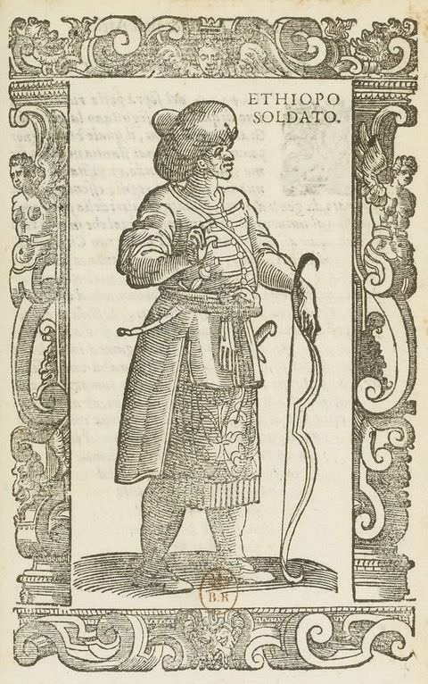 Page of a book. This black and white book illustration is surrounded by an ornately decorated frame featuring three-dimensional, organic shapes. Within the frame stands a figure dressed in a smart, fitted jacket and long skirt, with a long bow in one hand that rests on the ground. Text on the upper right of the image reads ‘ETHIOPO SOLDATO.’