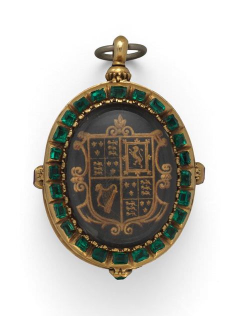 Colour photograph. The case of an oval miniature is photographed with its lid closed shut to reveal the exterior decoration. The inner oval features a heraldic, gold logo, while the rim of the oval is encircled with green jewels.