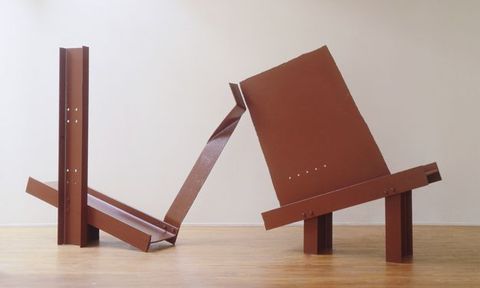 Colour photograph. Documentation of an abstract sculpture made from brown metal, situated within a gallery space with varnished wood floors and white walls.